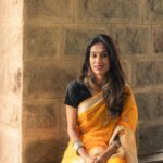 Portrait of an Indian woman in a yellow saree sitting indoors with a warm smile.